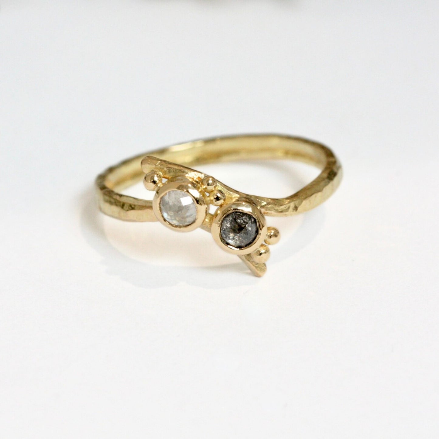Black rose cut diamond set next to a white rose cut diamond, bezel set on a hand forged 18 carat crossover band and gold granulation.