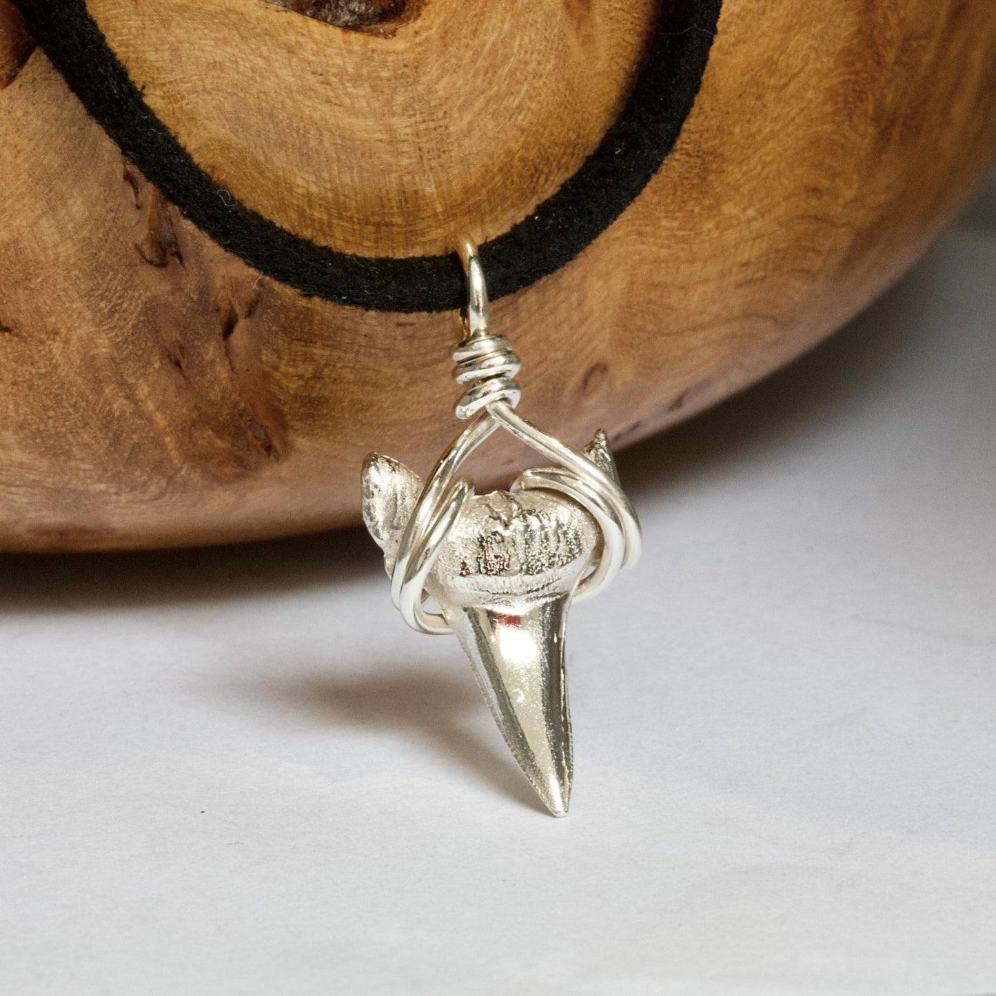 Silver sharks tooth pendant on a black faux suede thong against a wooden background.