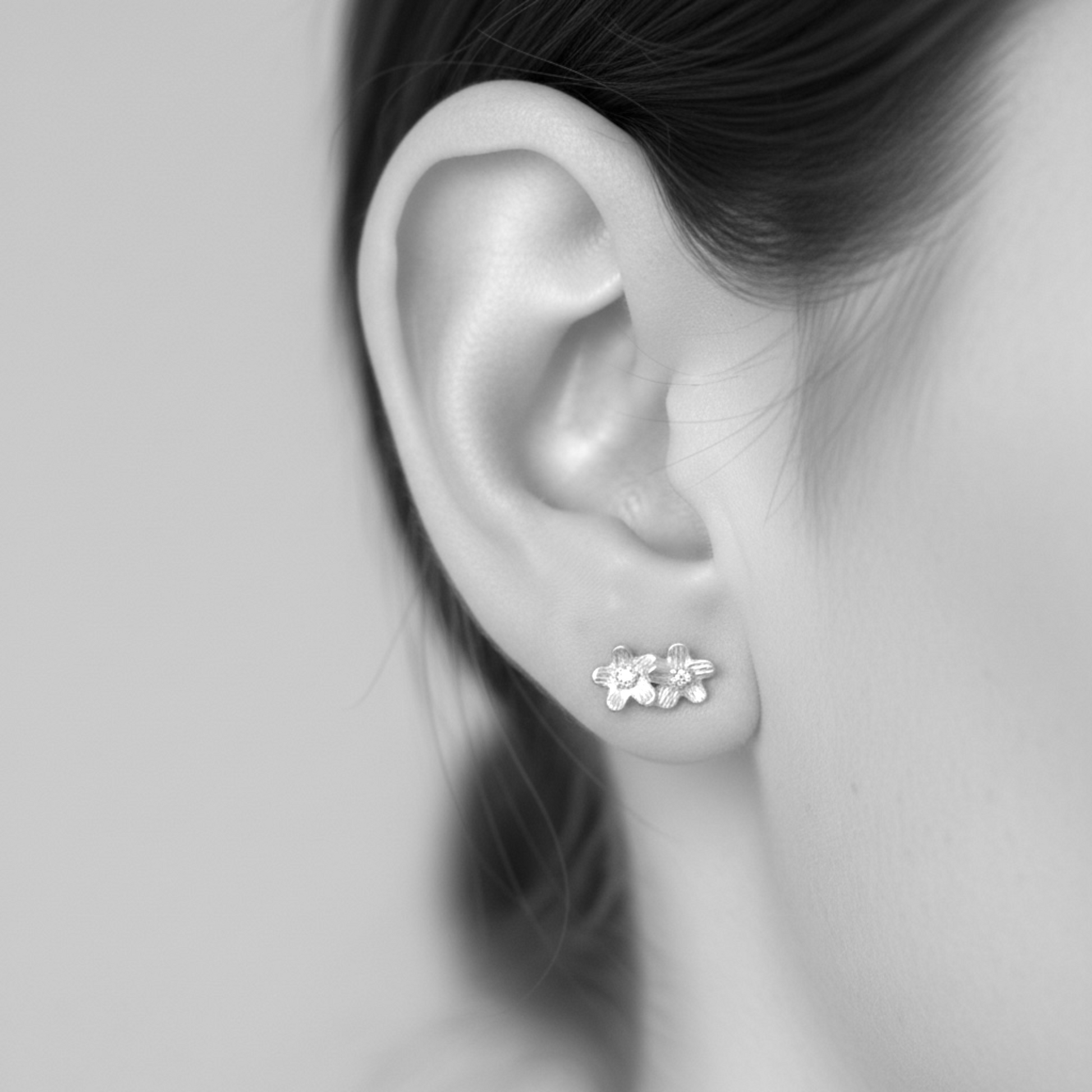 Close-up of an ear wearing a floral stud earring on a neutral background