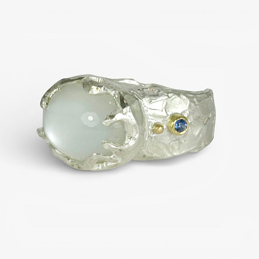 Sterling silver Celestial Ring with a large cabochon moonstone, featuring two 18ct gold accent set with blue sapphires and delicate fused gold details. Hand-carved organic shape with textured finish