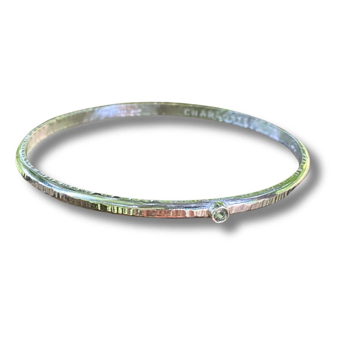 A hammered sterling silver bangle bracelet with a small round peridot gemstone accent on the front, shown on a white background with a soft drop shadow.