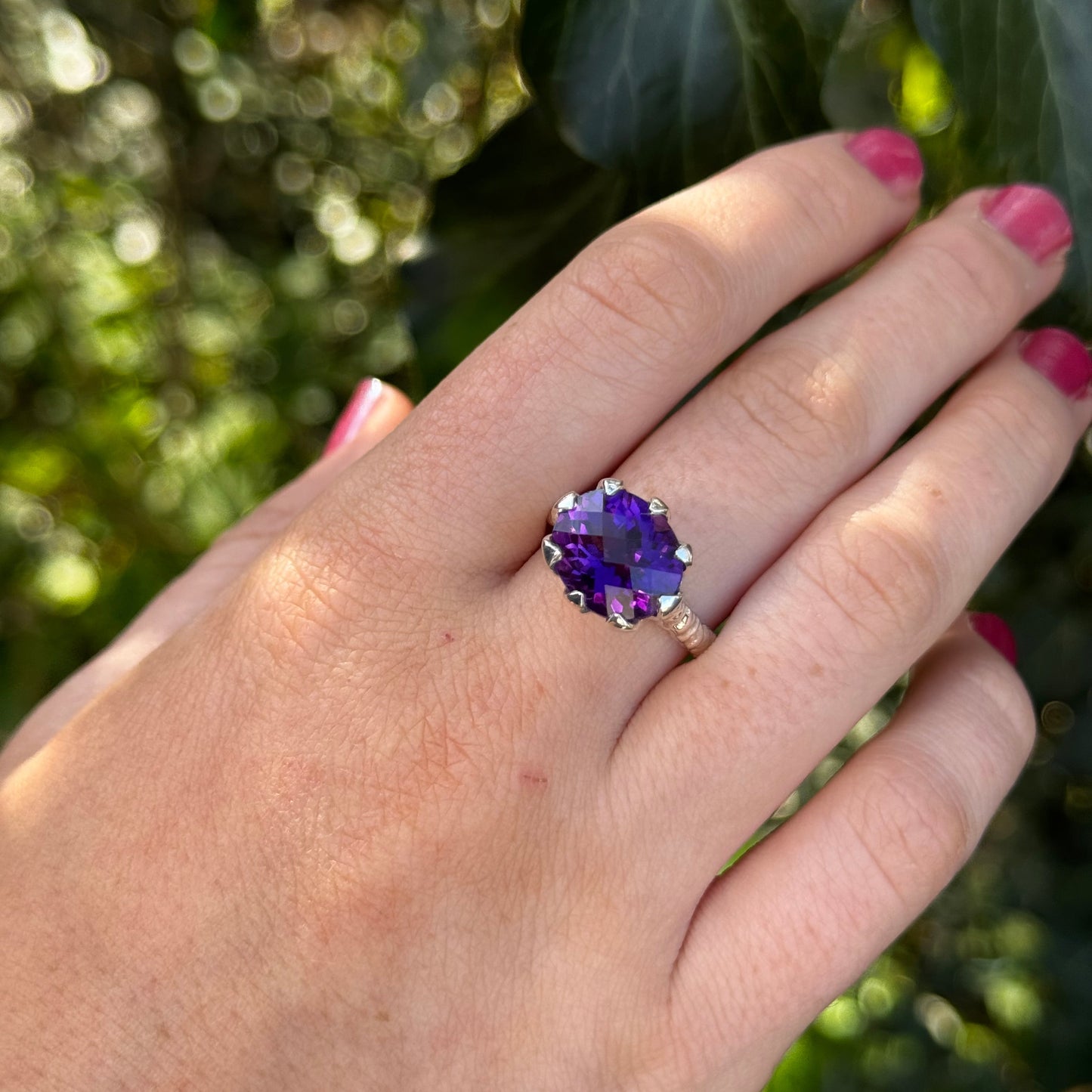 Hand-carved sterling silver ring with a high tulip petal-style bezel holding a dark purple oval chequerboard-cut amethyst, sculptural carved shank and elegant raised setting.