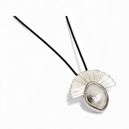 Inspired by wild landscapes and quiet, earthy beauty, this handcrafted silver pendant features a rustic rose-cut sapphire cradled in organic, sculpted metal. Its monochrome palette of cool silver and misted stone evokes mountain horizons and soft morning light, while the textured silver fan rises like a quiet sun over the landscape.