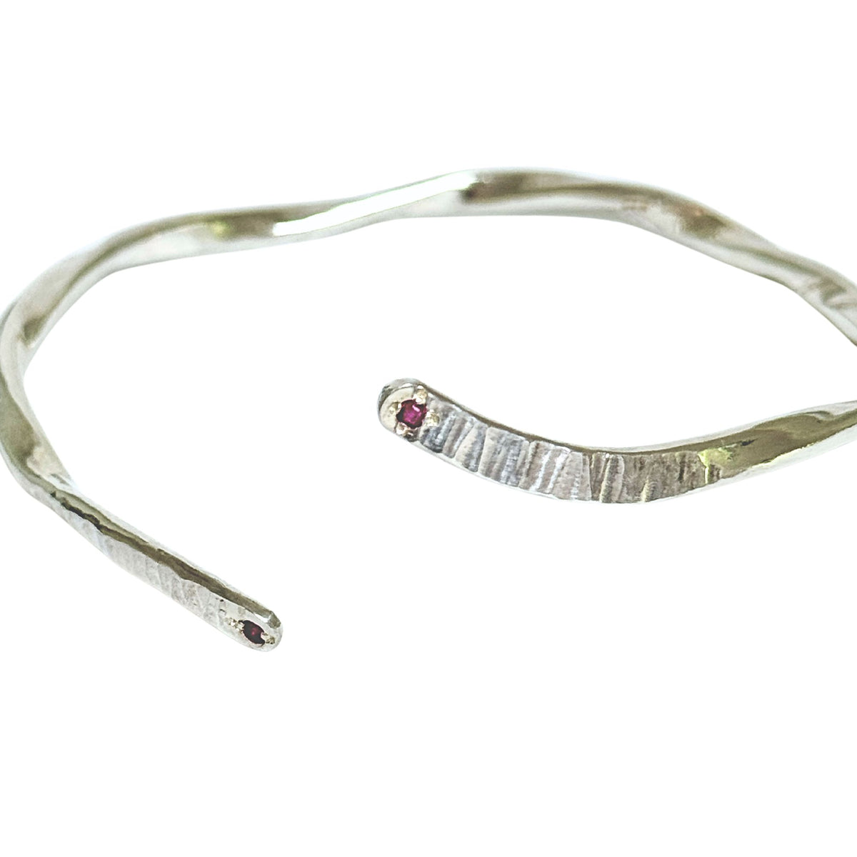 A textured sterling silver open cuff bracelet with two small round red ruby accents, shown on a plain white background.