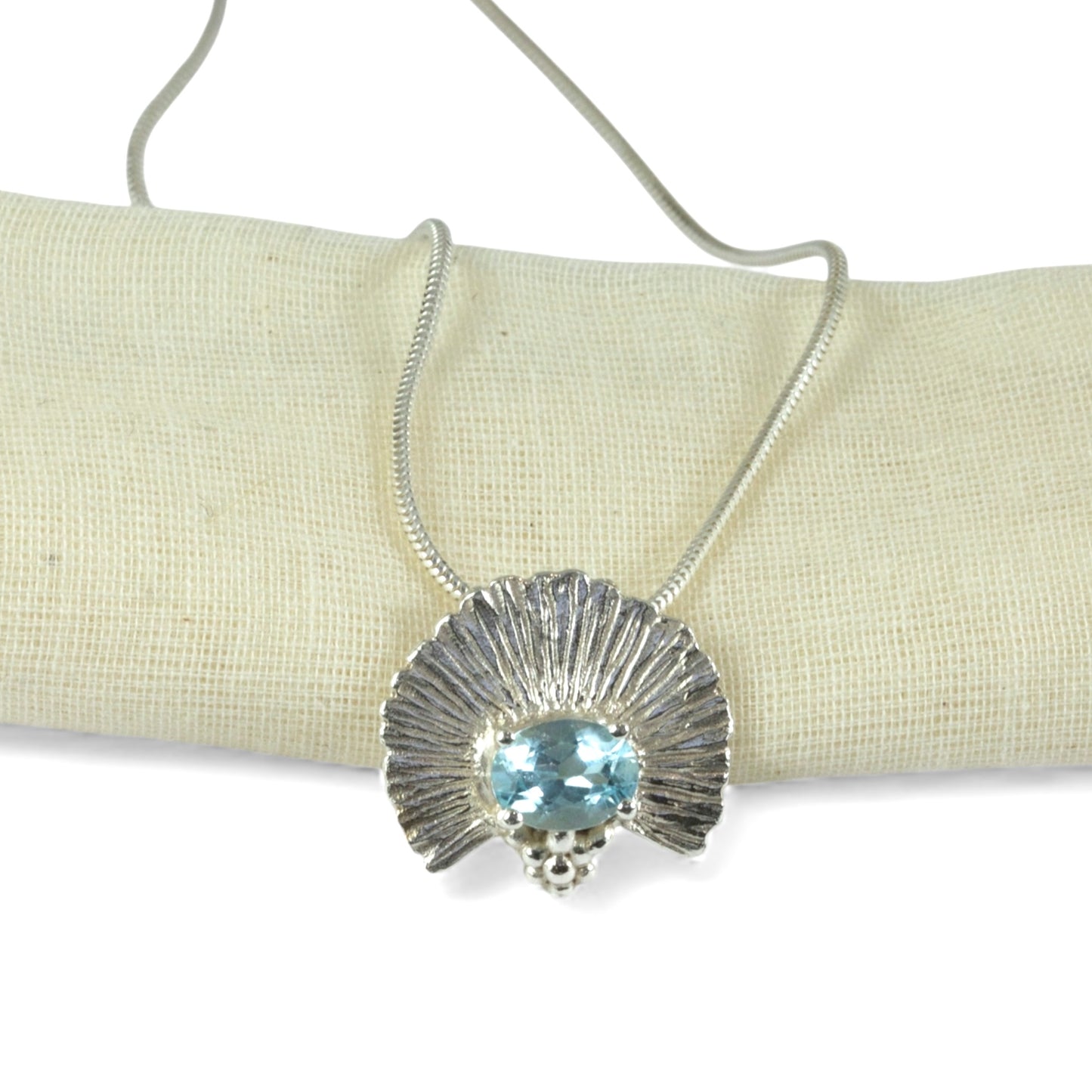 Silver necklace with a blue gemstone pendant on a beige fabric background