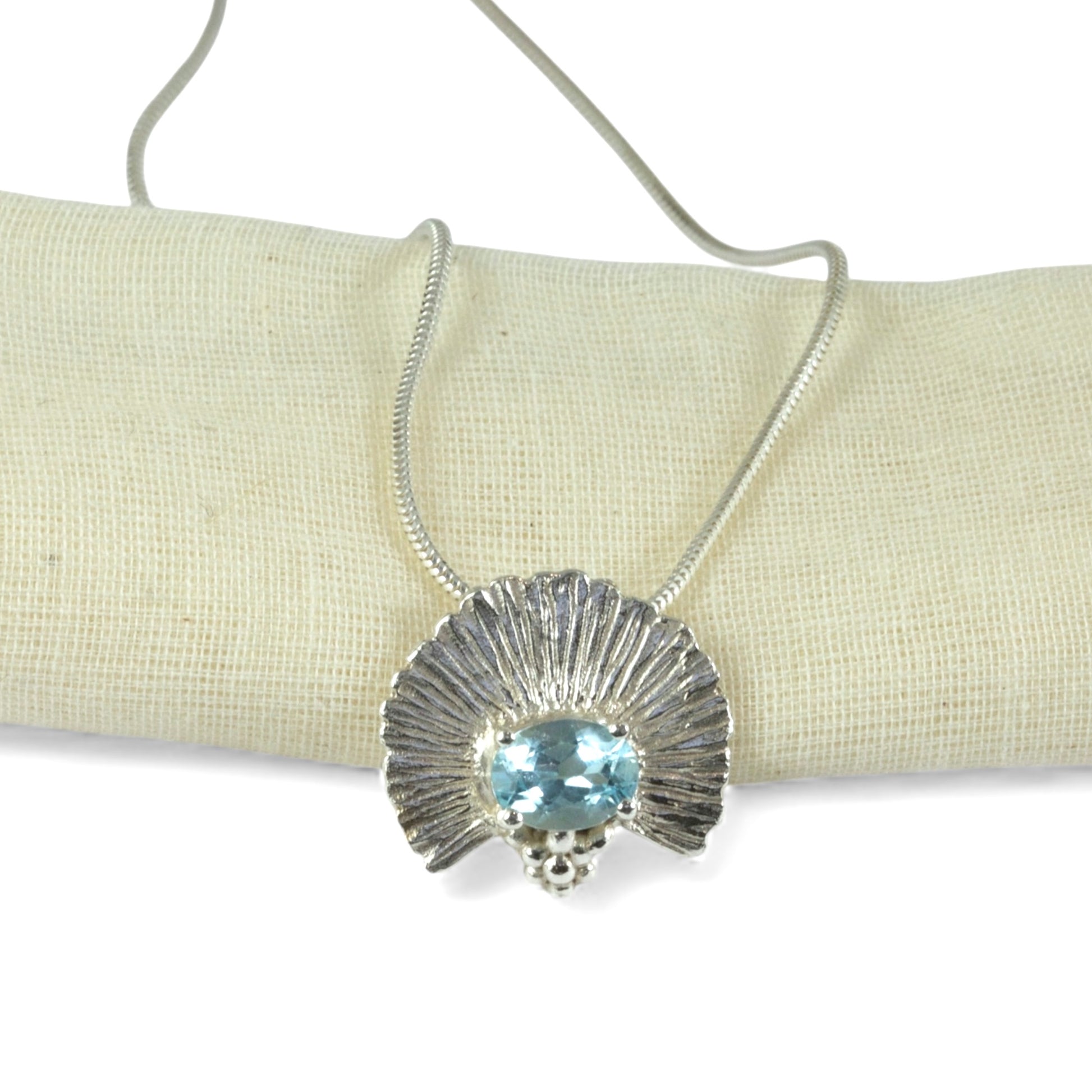 Silver necklace with a blue gemstone pendant on a beige fabric background