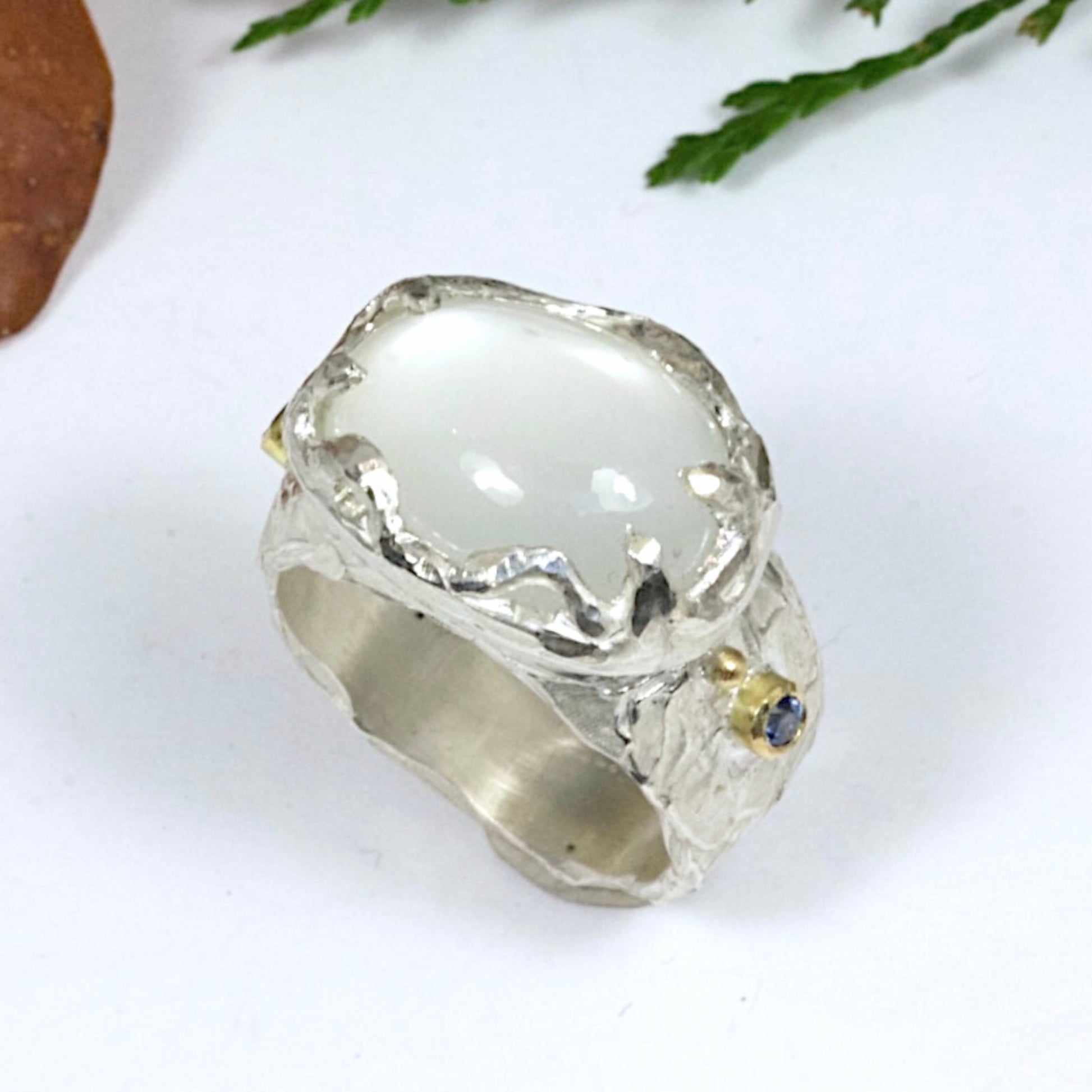 Sculptural sterling silver ring set with a large oval cabochon moonstone. Blue sapphires and 18 carat gold accents on the sides of the ring.