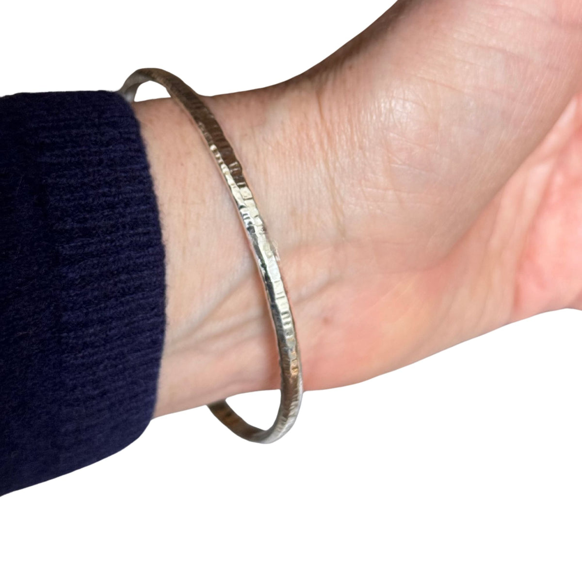 A hammered silver metal bangle bracelet worn on a person's wrist, shown against a plain white background with a dark navy sleeve visible.