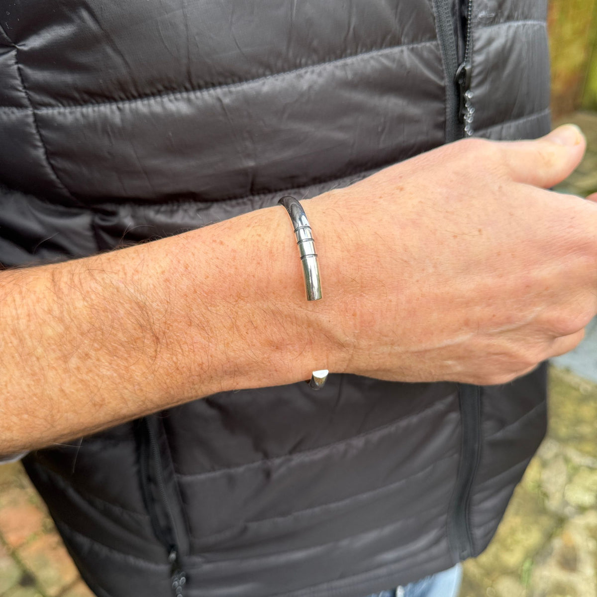 A close-up of a person's forearm wearing a polished silver-cuff bracelet, shown against a black puffer jacket.